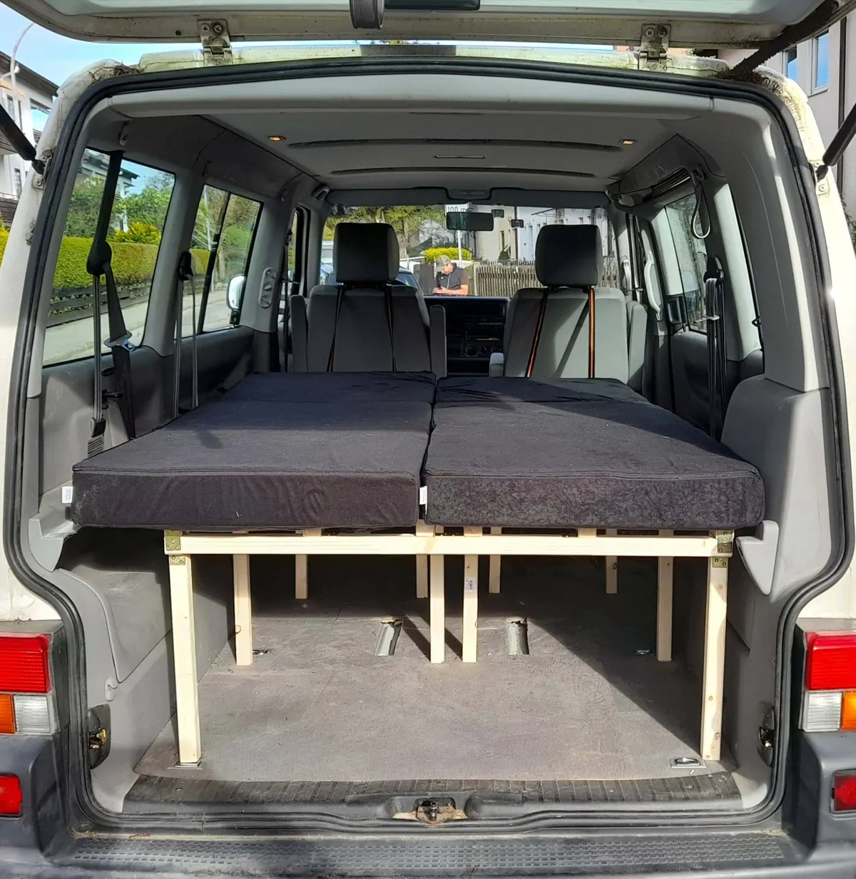 Ausgeklapptes Doppelbett auf einem Holzrahmen im Innenraum eines VW T4